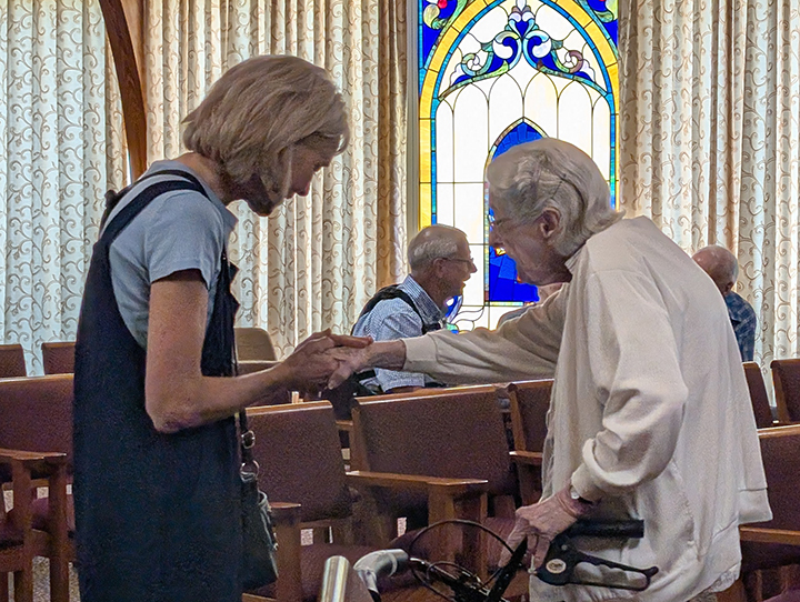 Mary holds a senior living resident's hand while praying